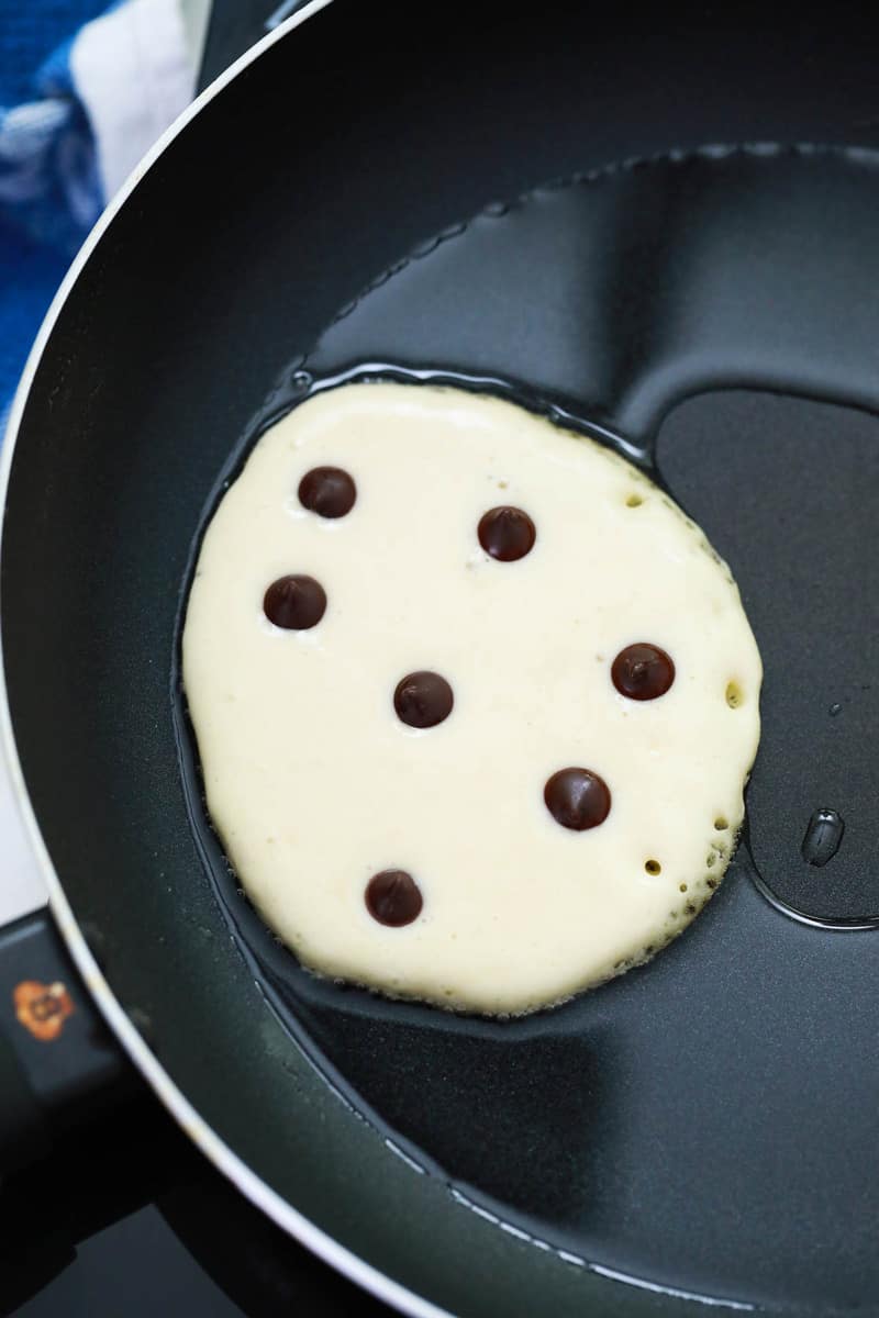 close up shot of pancake on the frying pan with chocolate chips on top