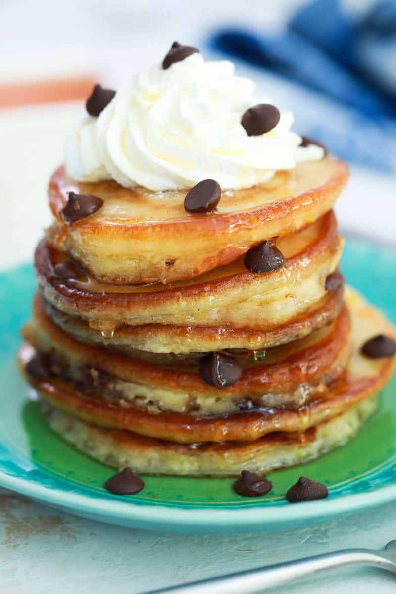 Chocolate Chip Pancakes stacked on a plate topped with whipped cream and chocolate chips