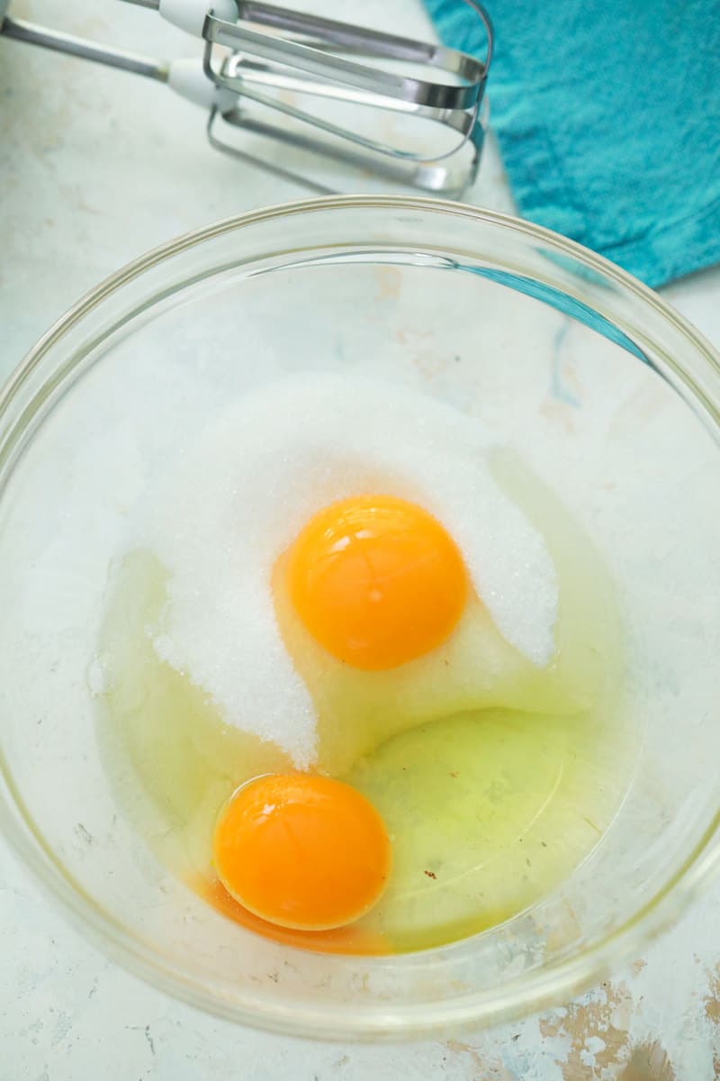 mixing sugar and eggs in glass bowl with electric hand mixer