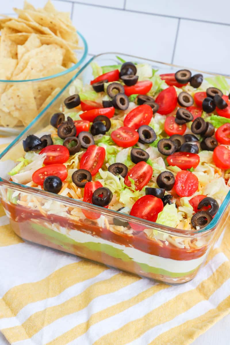 close up photo of 7 layer dip with tortilla chips in a bowl behind it