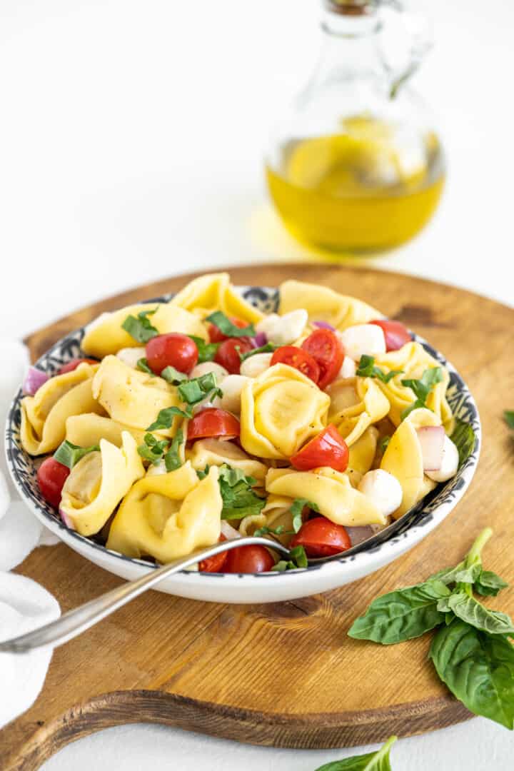 tortellini pasta salad in a bowl on a wooden serving board