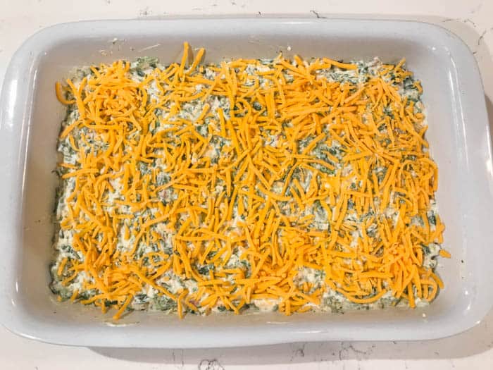 adding the dip to the casserole dish and topping with cheddar cheese