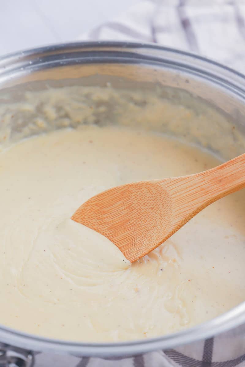 closeup of alfredo sauce mixing with wooden spoon.
