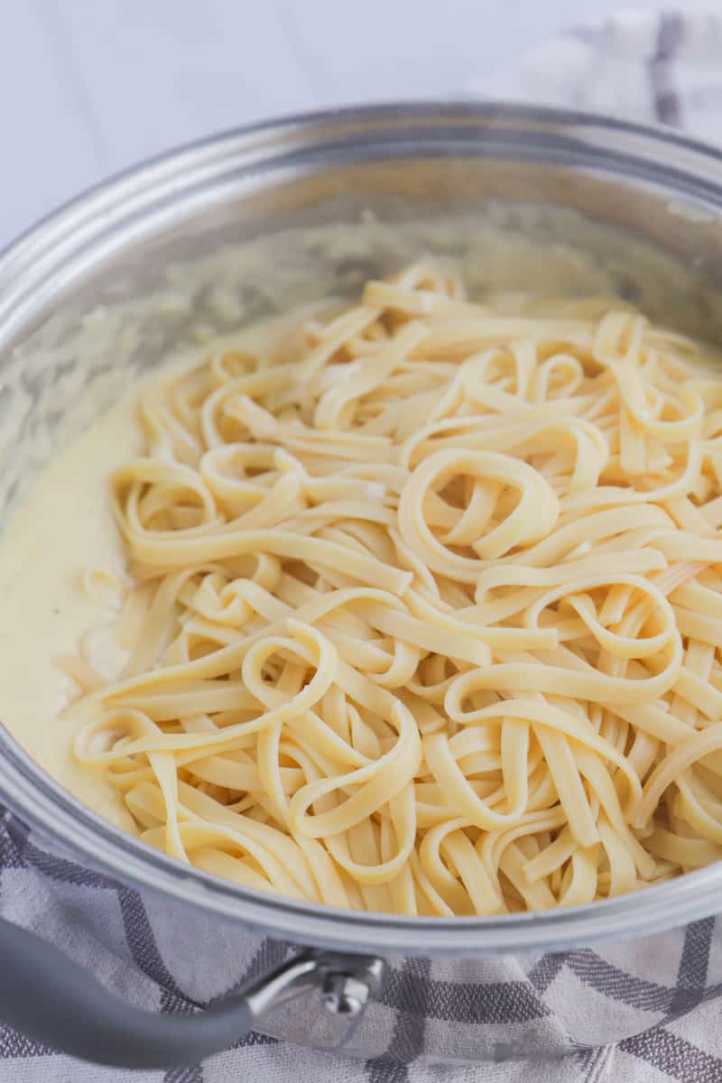 adding cooked fettuccini to the alfredo sauce.