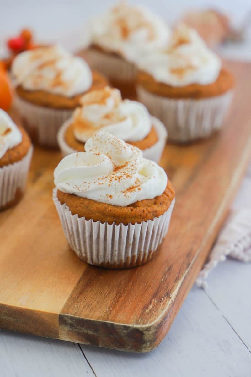 closeup of pumpkin cupcakes on wooden board topped with whipped cream