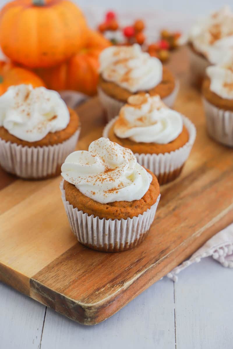 Pumpkin Pie Cupcakes topped with whipped cream on wooden serving board