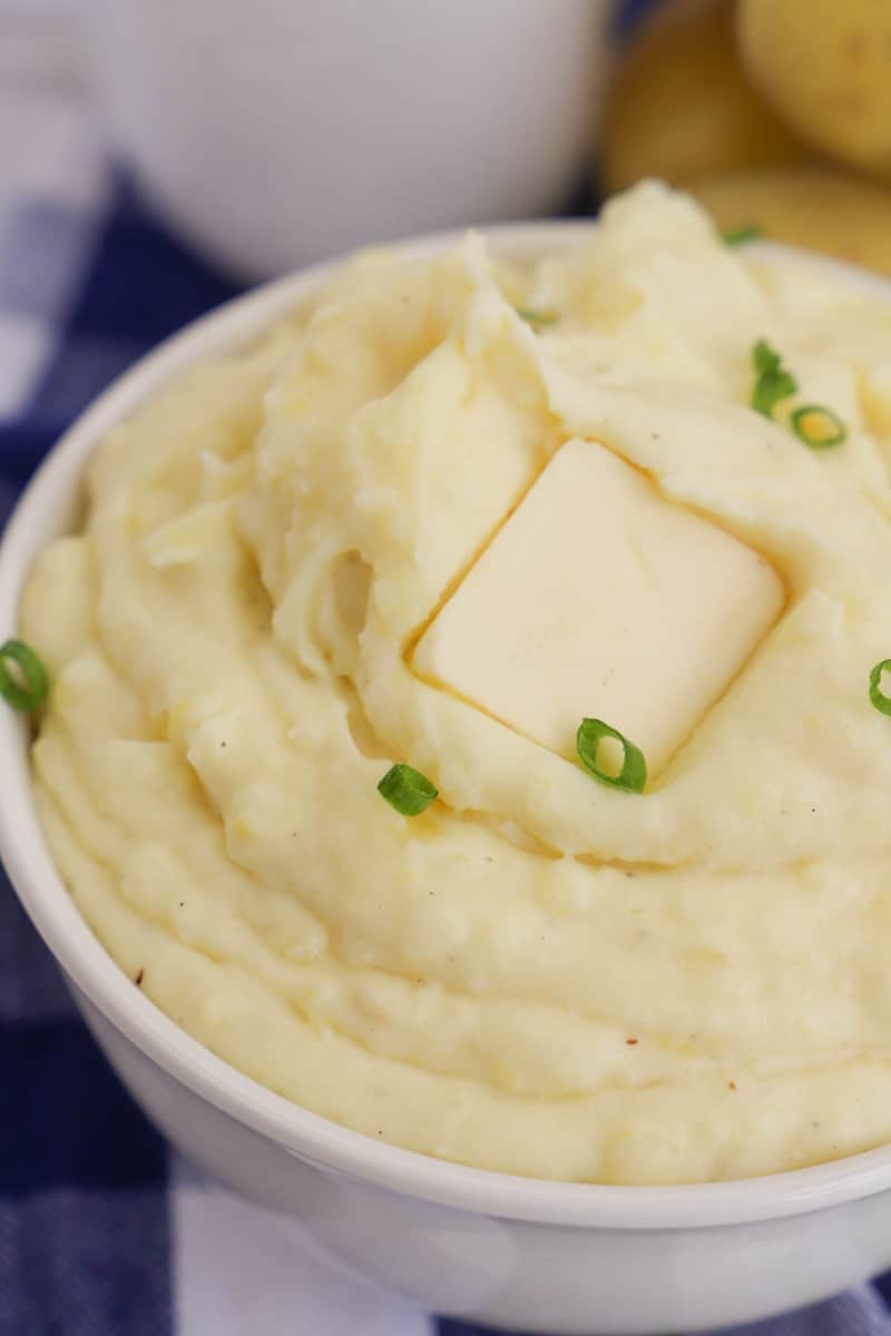close up of cream cheese mashed potatoes in white bowl with butter on top