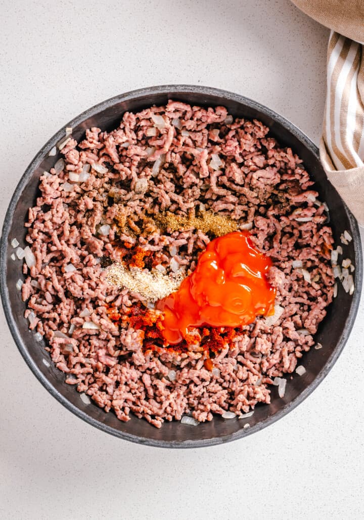 adding in seasoning and tomato sauce to the meat