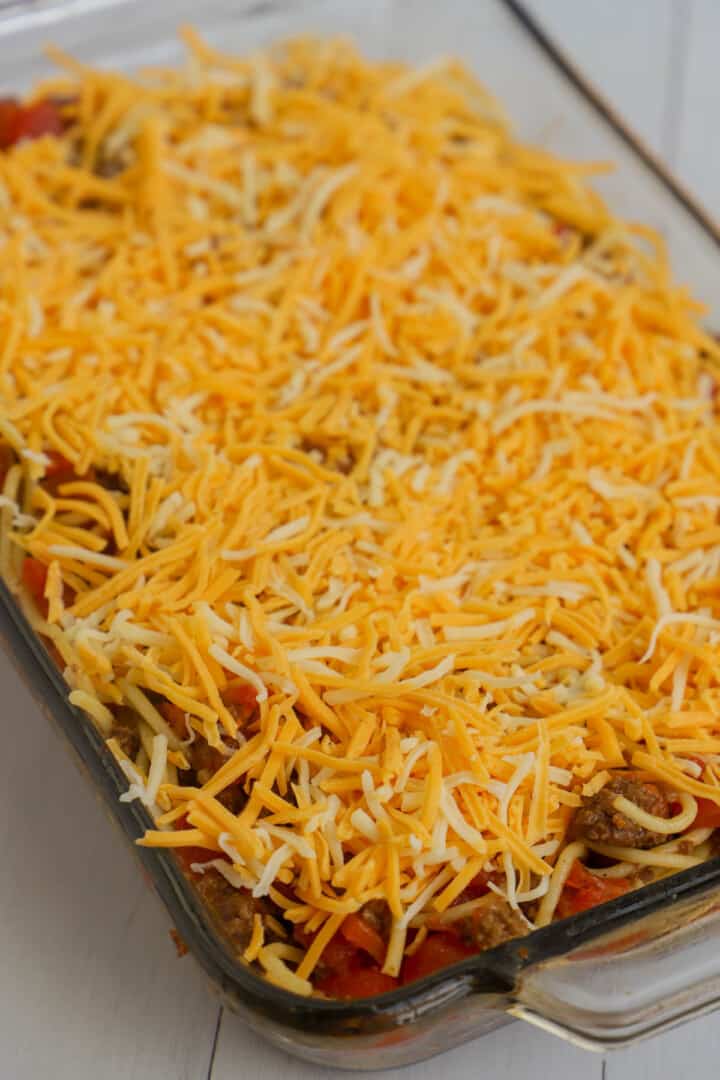 topping taco spaghetti casserole with cheese before baking