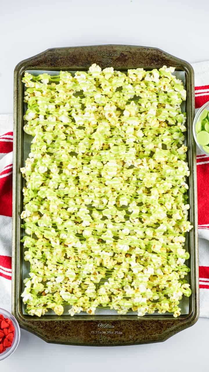 green melted candy drizzled on popcorn on baking sheet