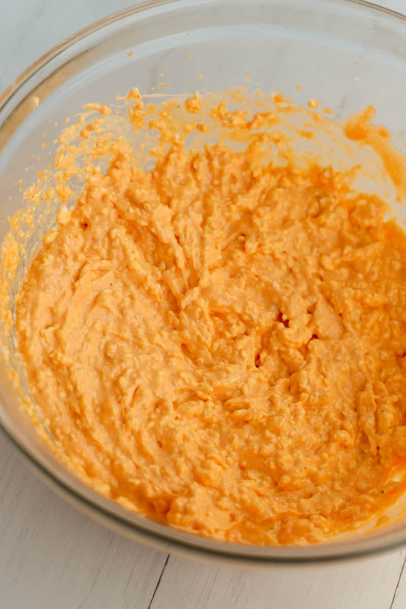 mixing cream cheese and buffalo sauce in a glass bowl