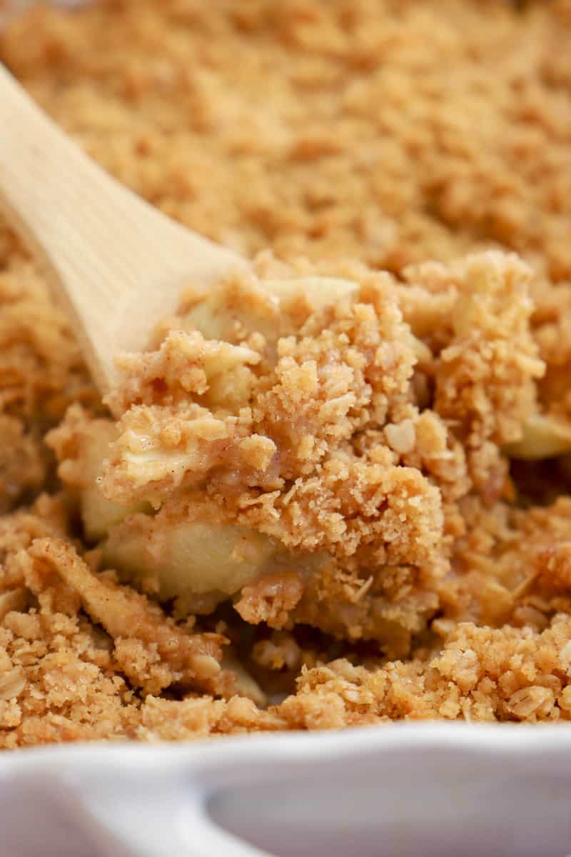 baked apple crisp being scooped out with wooden spoon