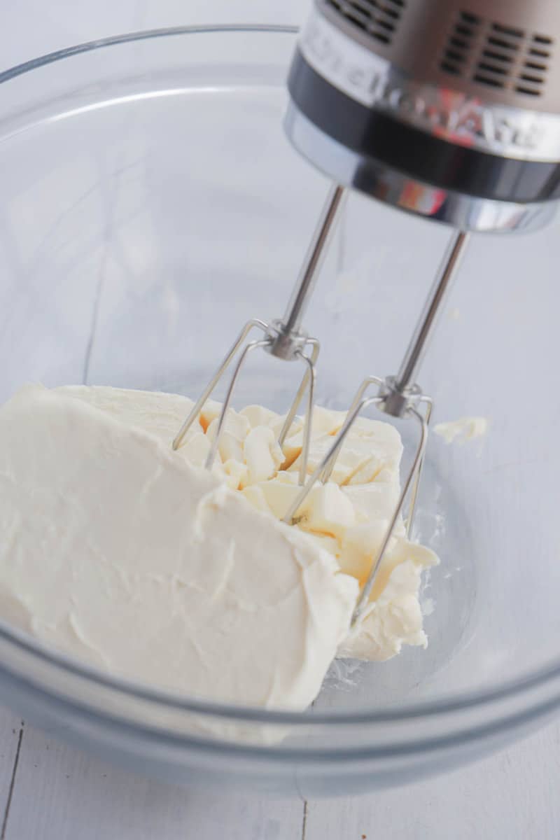 mixing cream cheese in a glass bowl with a hand mixer