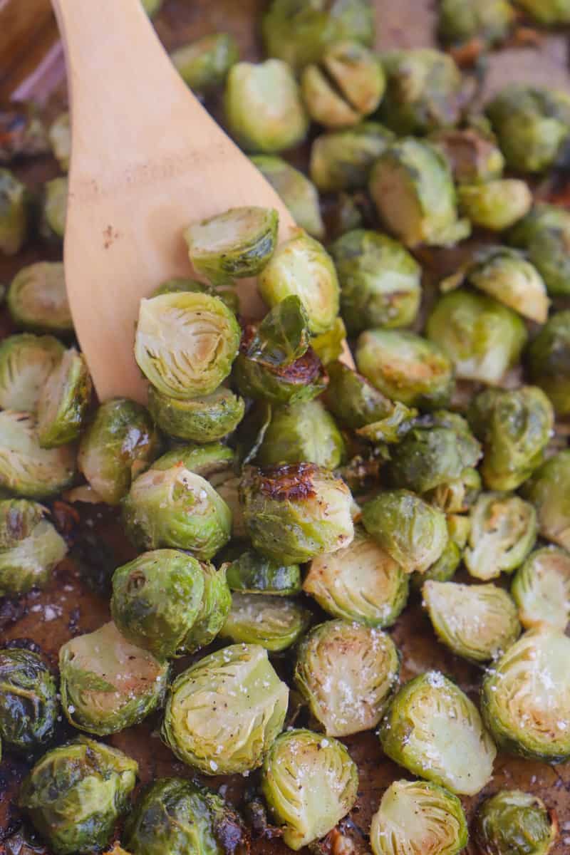 serving Brussel sprouts off baking sheet with wooden spoon