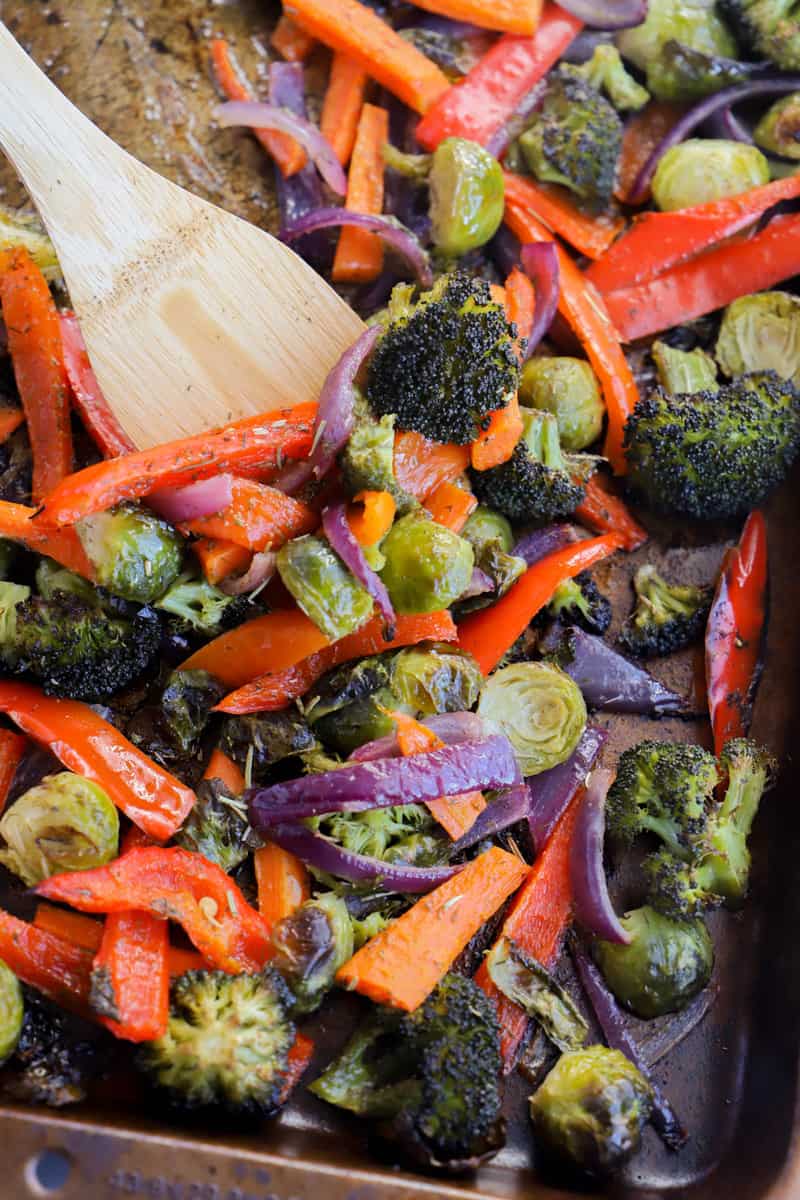 roasted vegetables being scooped off baking sheet