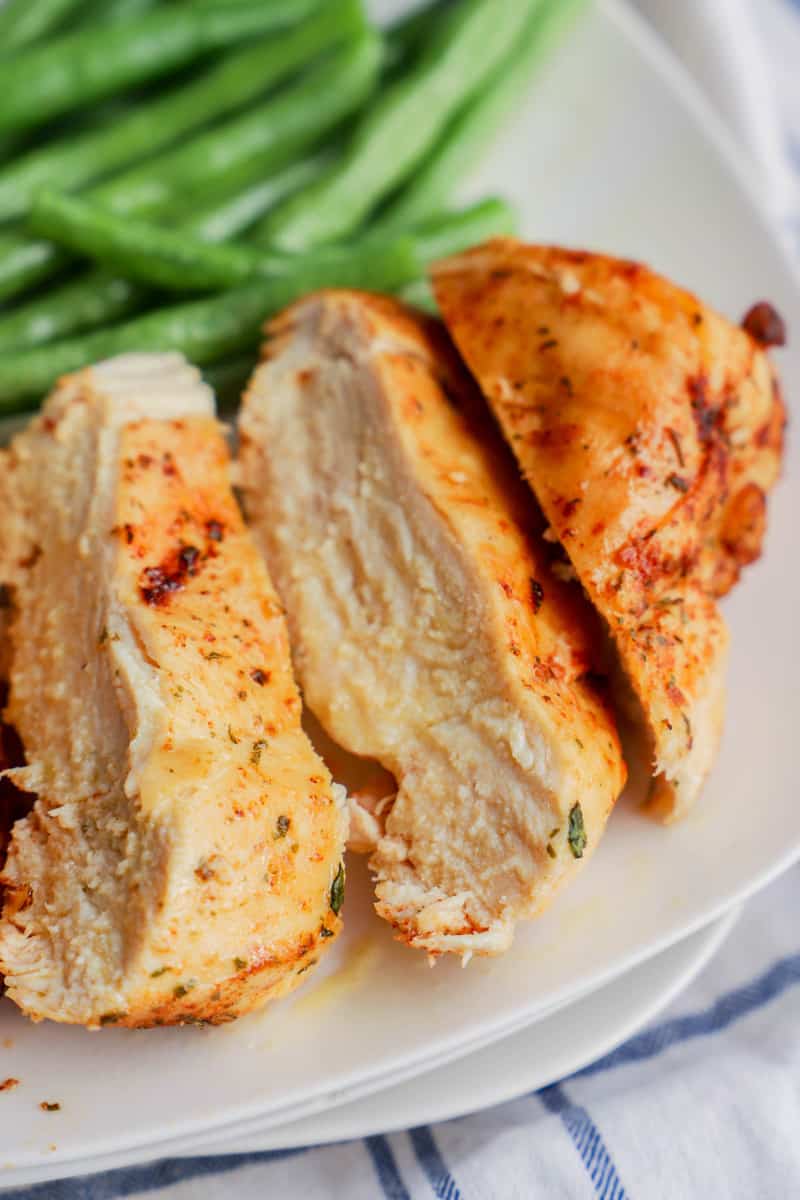close up of sliced chicken breast on white plate with green beans