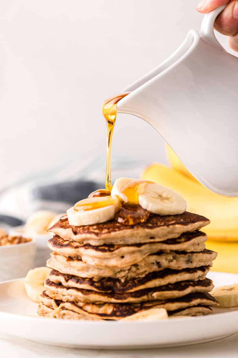 pouring syrup on top of a stack of the pancakes.