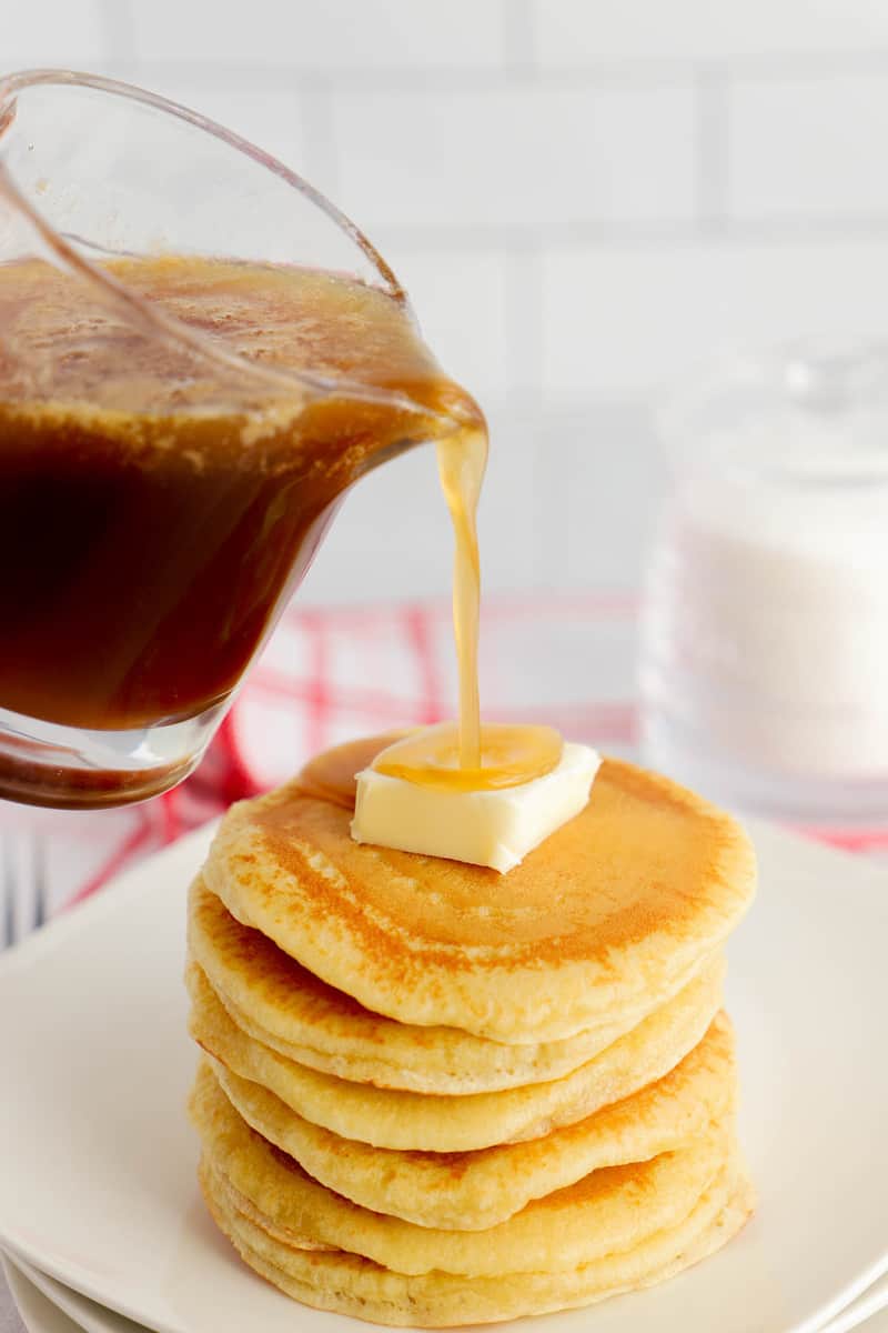 pouring homemade pancake syrup on top of a stack of pancakes