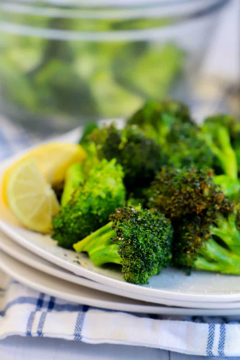 close up of broccoli on stacked white plates with lemon garnish