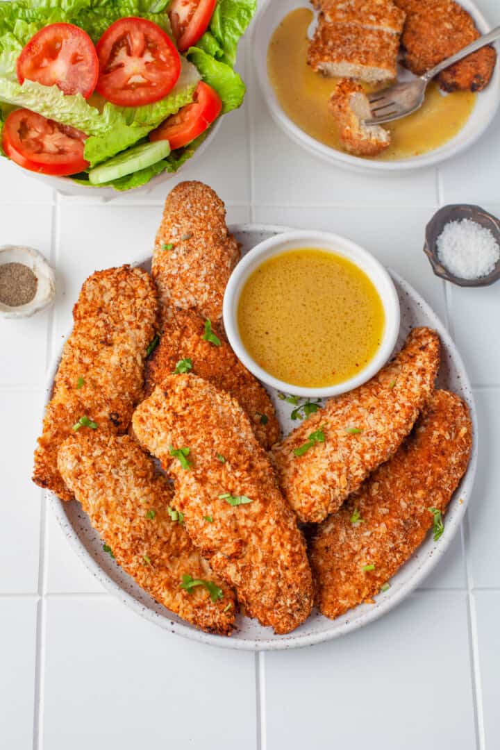 air fryer chicken tenders on white plate with honey mustard and salad