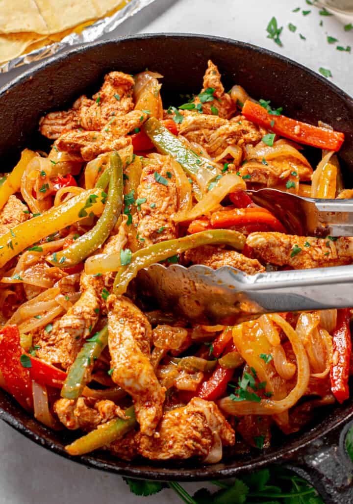 Chicken Fajitas in skillet being served with tongs.