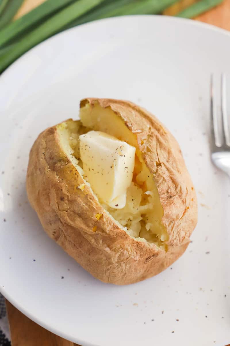 closeup of baked potato sliced open with butter in it on white plate