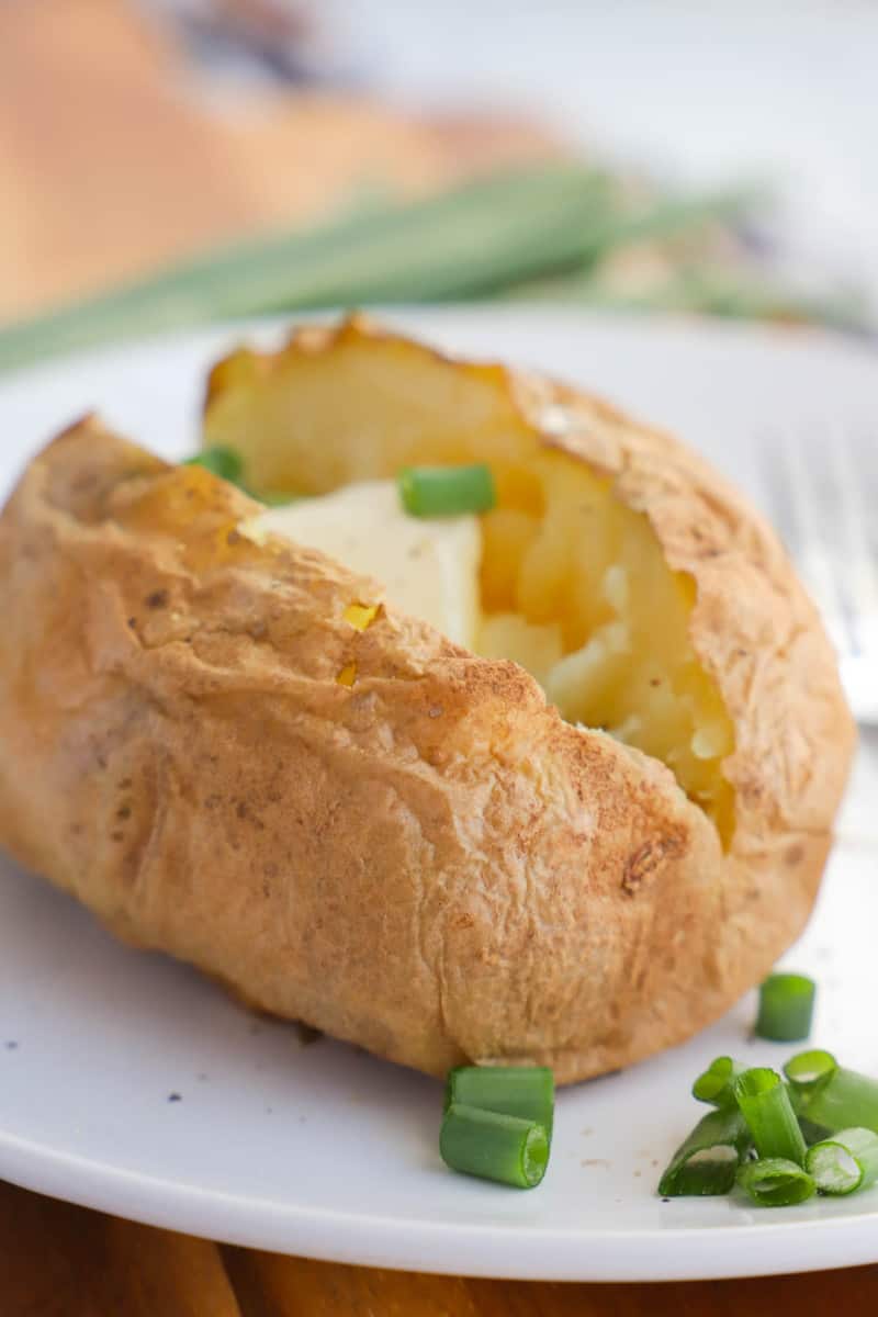 closeup of sliced baked potato with green onions and butter