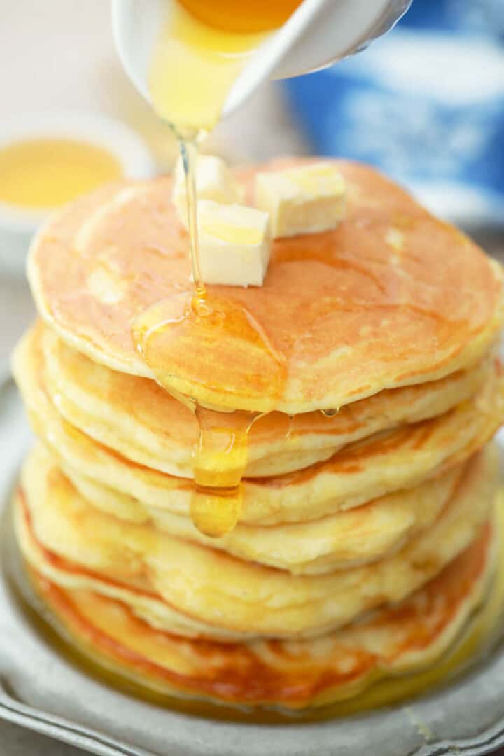 pouring syrup over a stack of pancakes