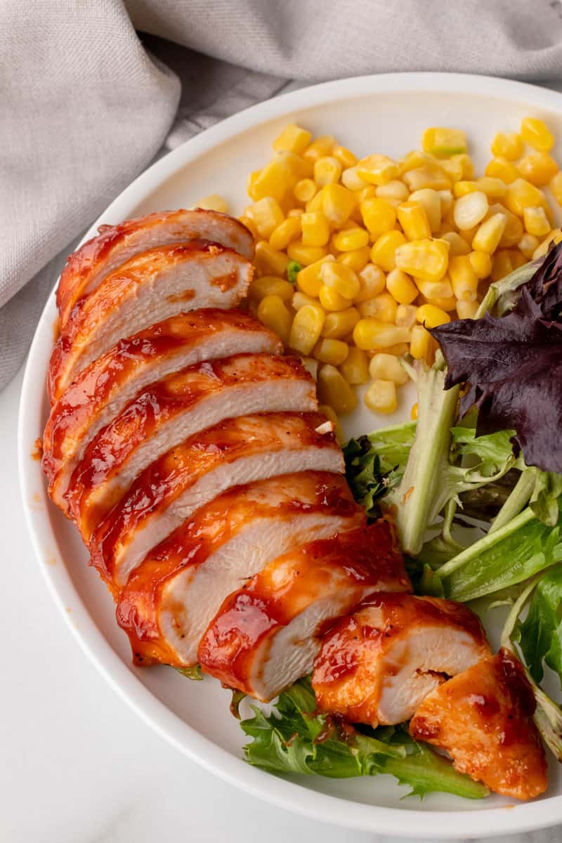 Baked BBQ Chicken on white plate with corn and salad