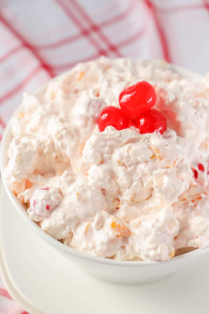 Ambrosia Fruit Salad in white bowl topped with cherries