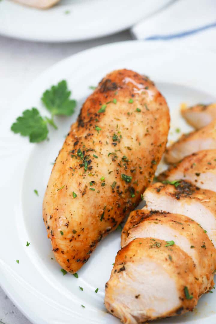 closeup of baked chicken breasts on white plate.