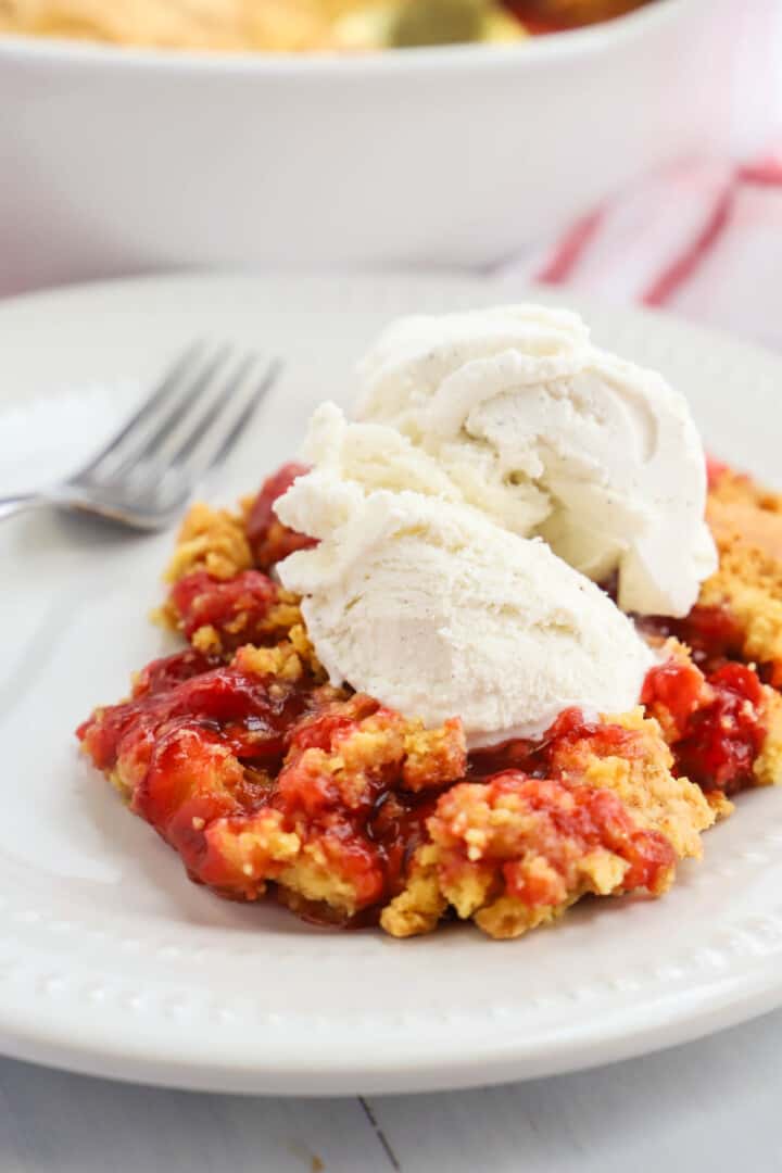 cherry dump cake on white plate with vanilla ice cream