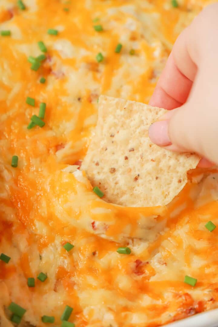 scooping out crack chicken dip with a tortilla chip