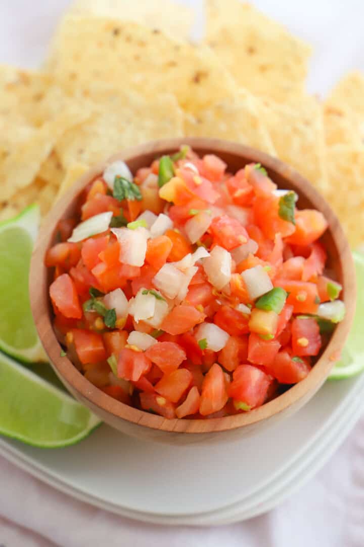 Pico de Gallo in wooden serving bowl with chips and lime slices