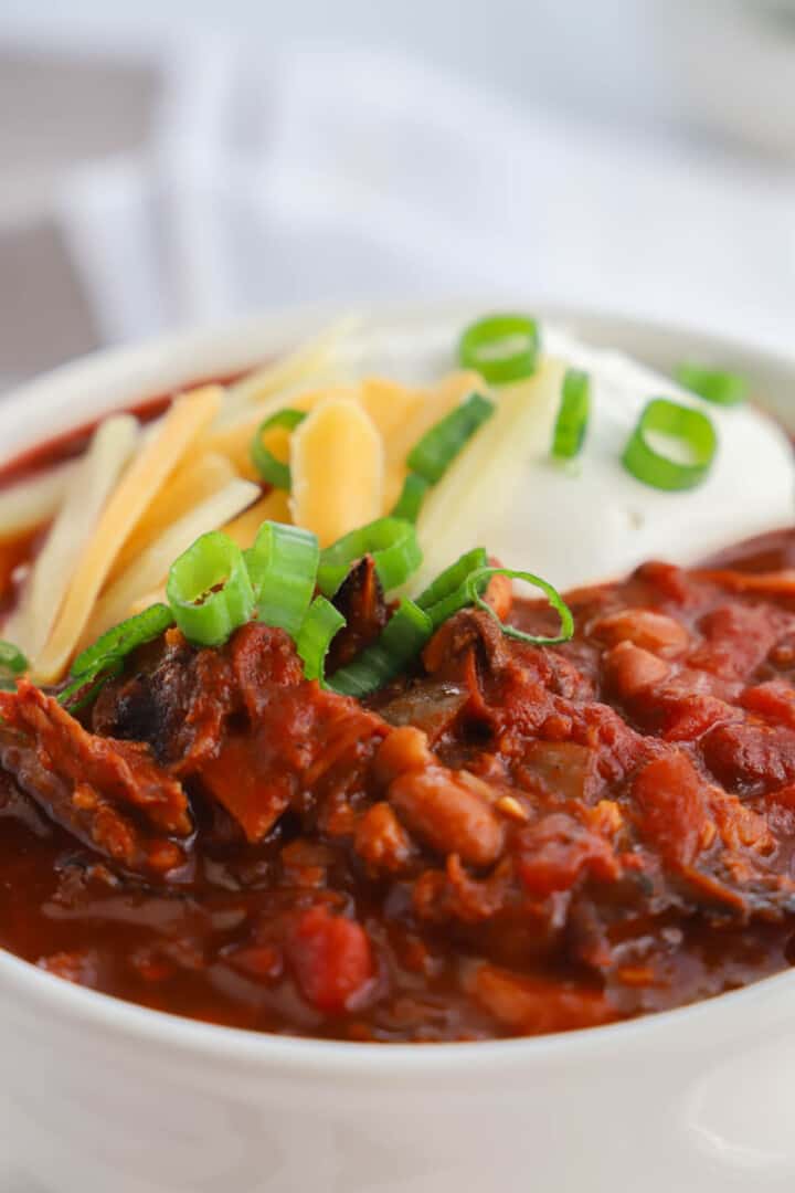 pulled pork chili in white bowl topped with cheese and sour cream