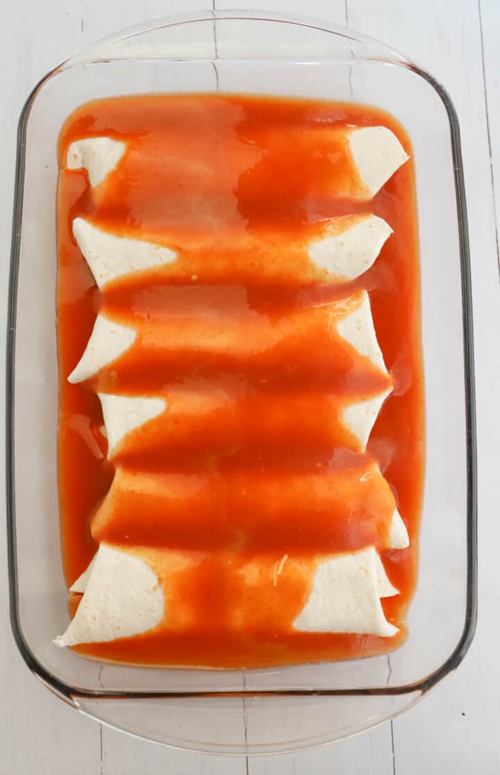 topping enchiladas in casserole dish with sauce
