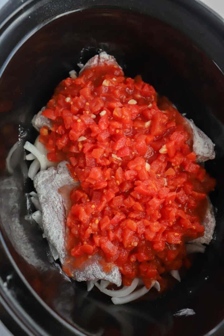 adding the tomato mixture to the slow cooker on top of the steak