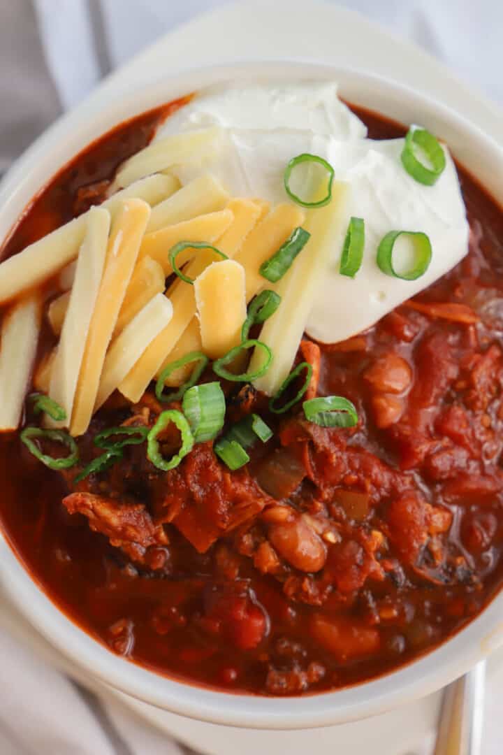 pulled pork chili in white bowl topped with cheese and sour cream