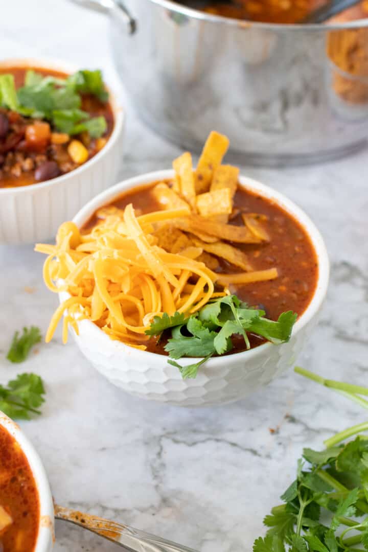 taco soup in white bowl topped cheese.