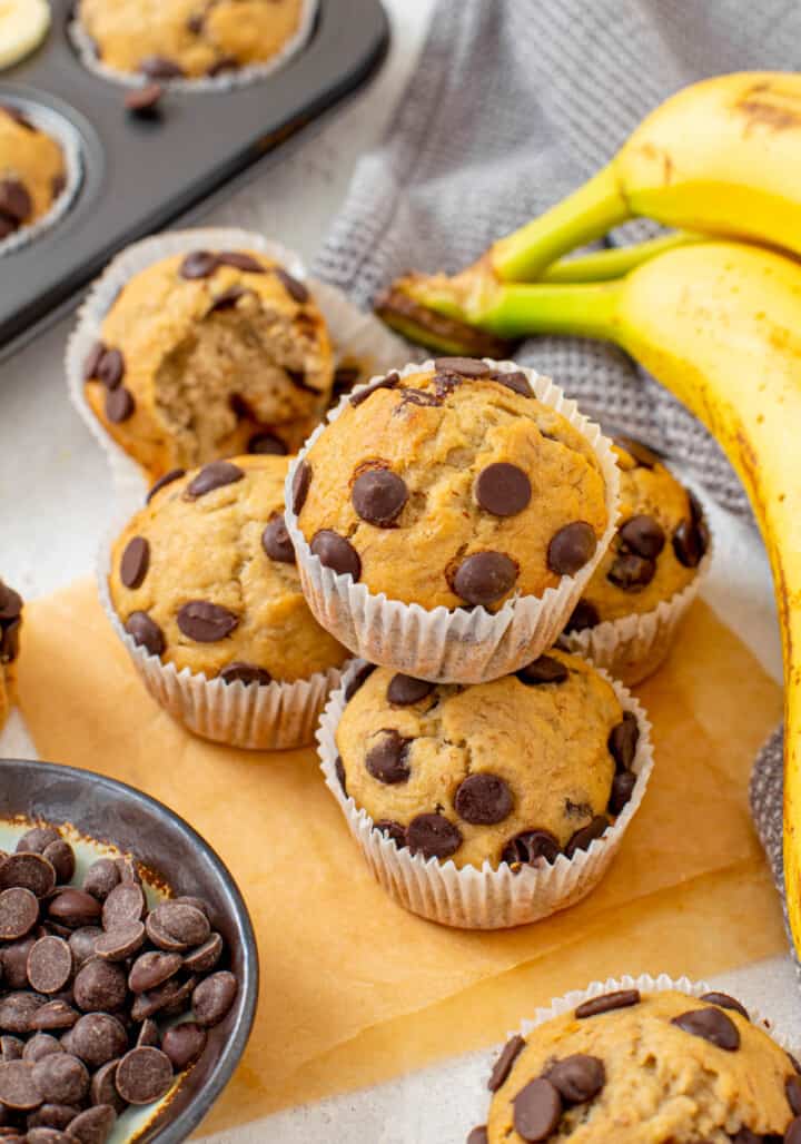 Banana Chocolate Chip Muffins stacked with bananas and chocolate chips in background