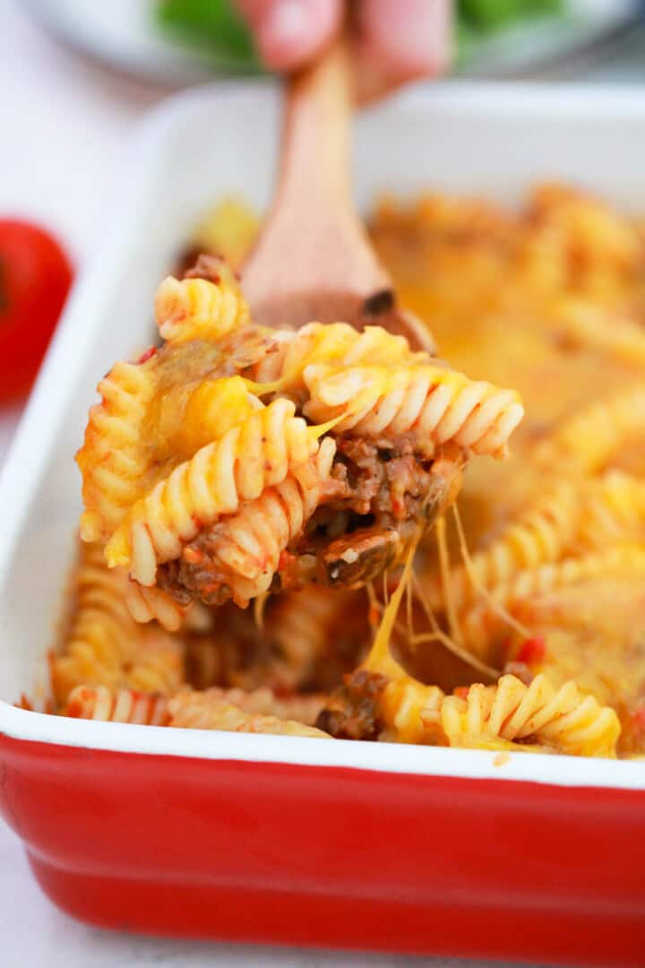 Cheeseburger Casserole in red casserole dish being scooped out