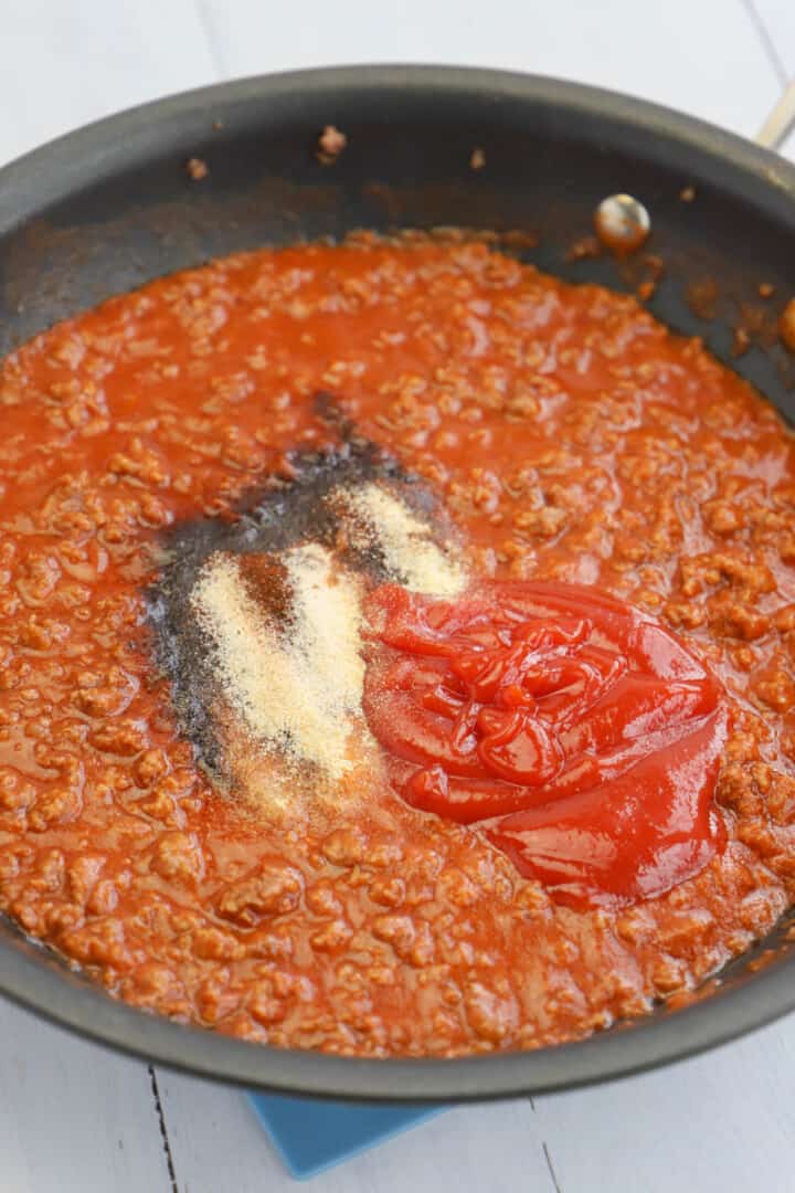 adding sauce and spices to the hot dog chili meat in pan