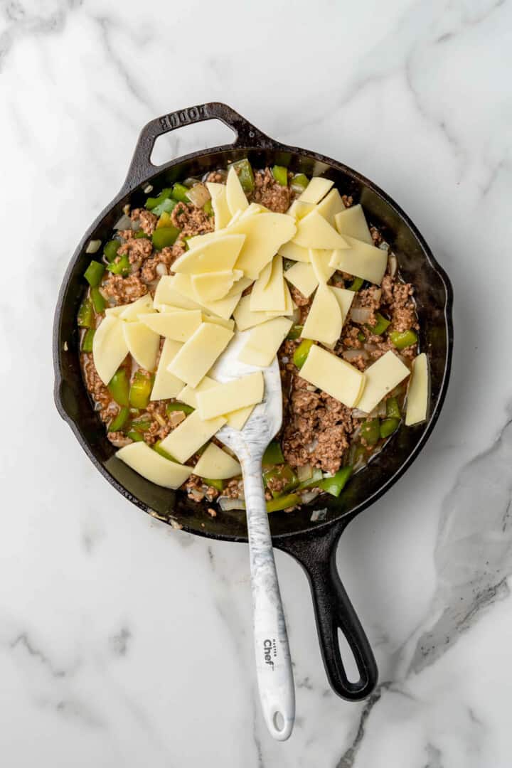 adding provolone cheese to the sloppy joes in the skillet