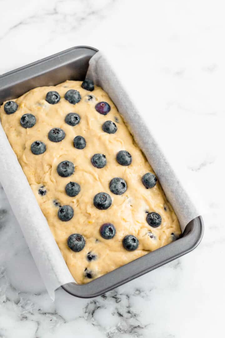 batter in bread pan topped with extra blueberries.