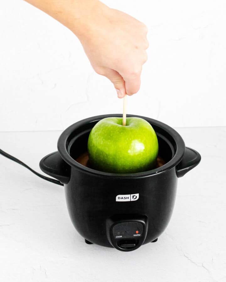 dipping caramel apple into slow cooker.