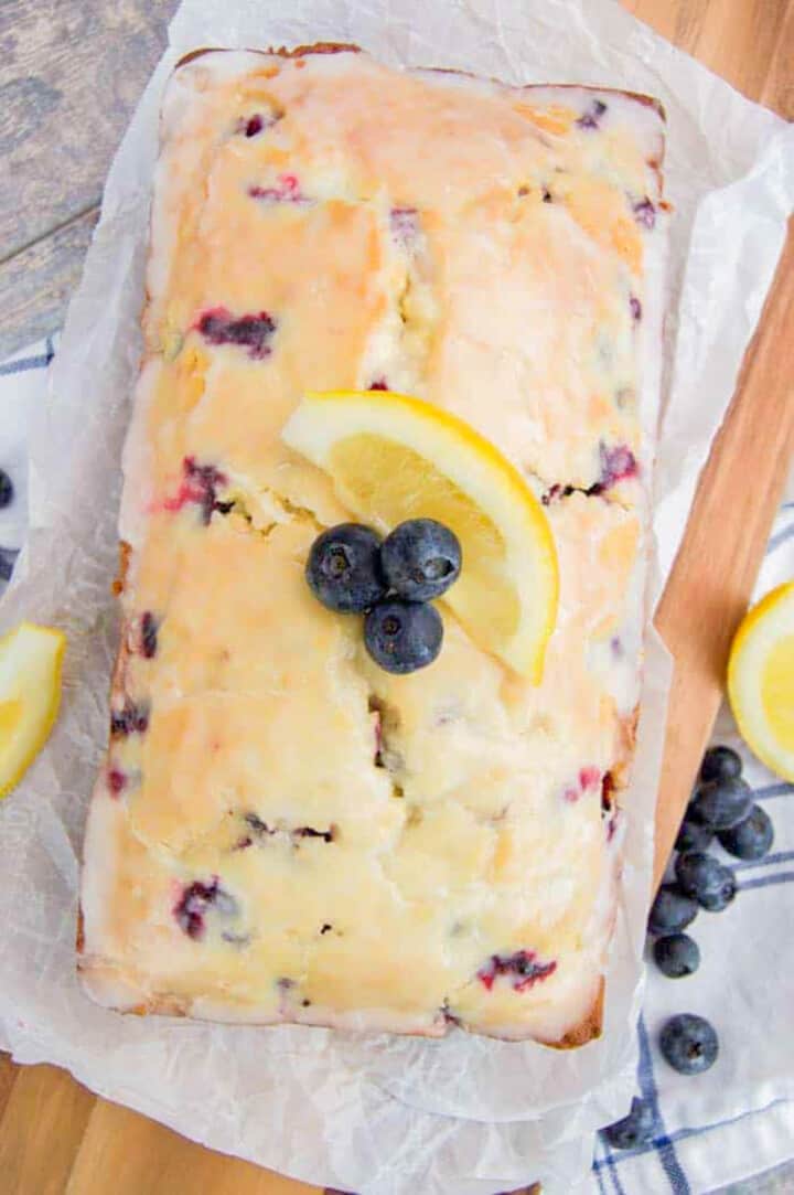 Blueberry Lemon Loaf on wooden board topped with blueberries and lemon slice.