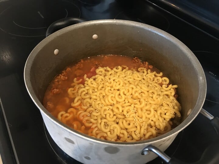 adding the noodles to the pan for the taco pasta.