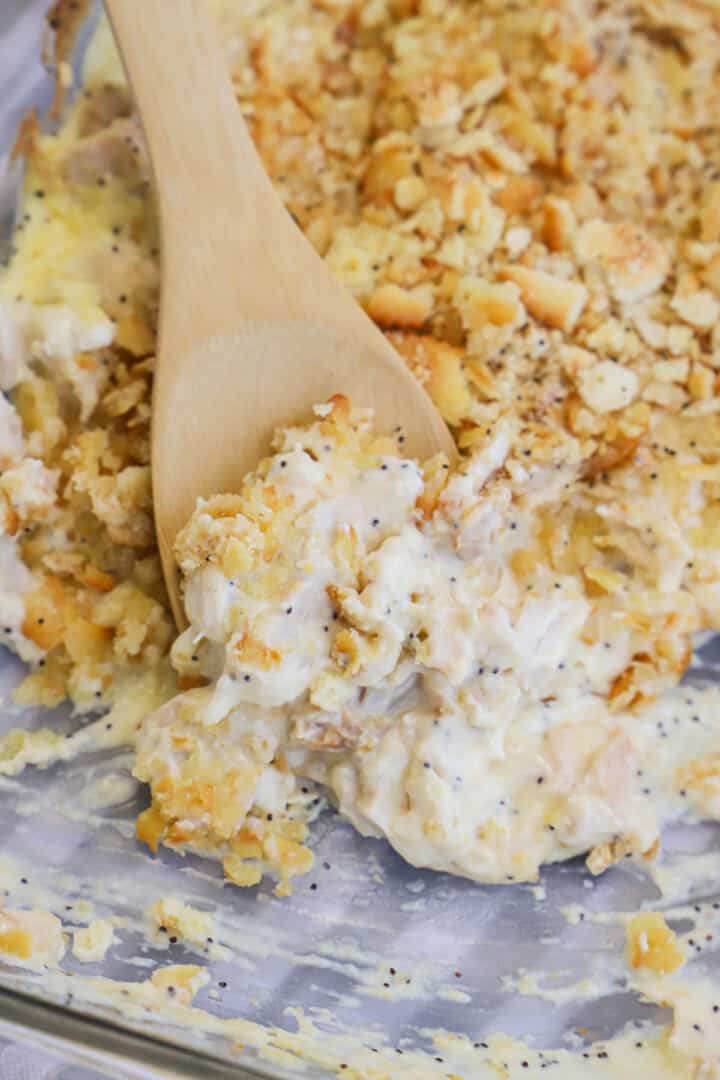 Poppy Seed Chicken Casserole in casserole dish being scooped out with wooden spoon.