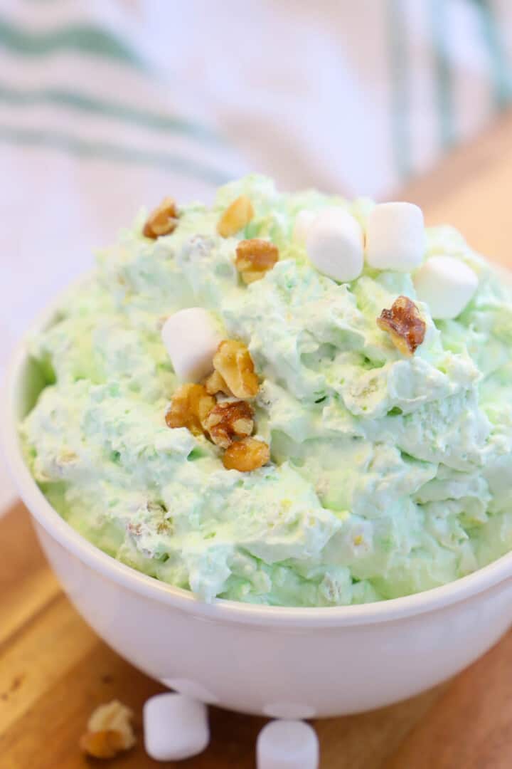 Watergate Salad in white bowl topped with pecans and marshmallows