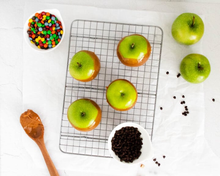 Top view of caramel apples with candies in bowls on the side.